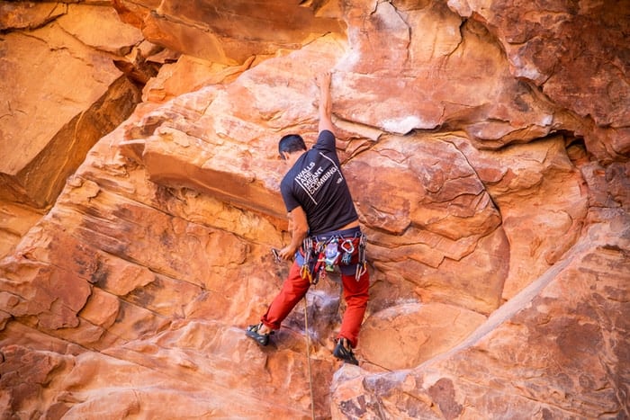 man in black t-shirt and orange shorts climbing brown rock formation during daytime