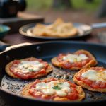 DIY campfire trail pizzas made with tortillas, sauce, and cheese cooked in a skillet outdoors.